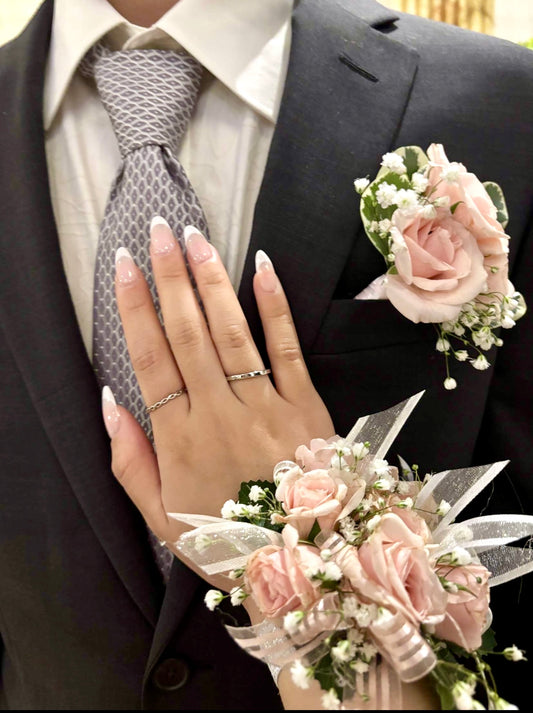Person wearing a dark suit with a floral wrist corsage and hand showing a ring.