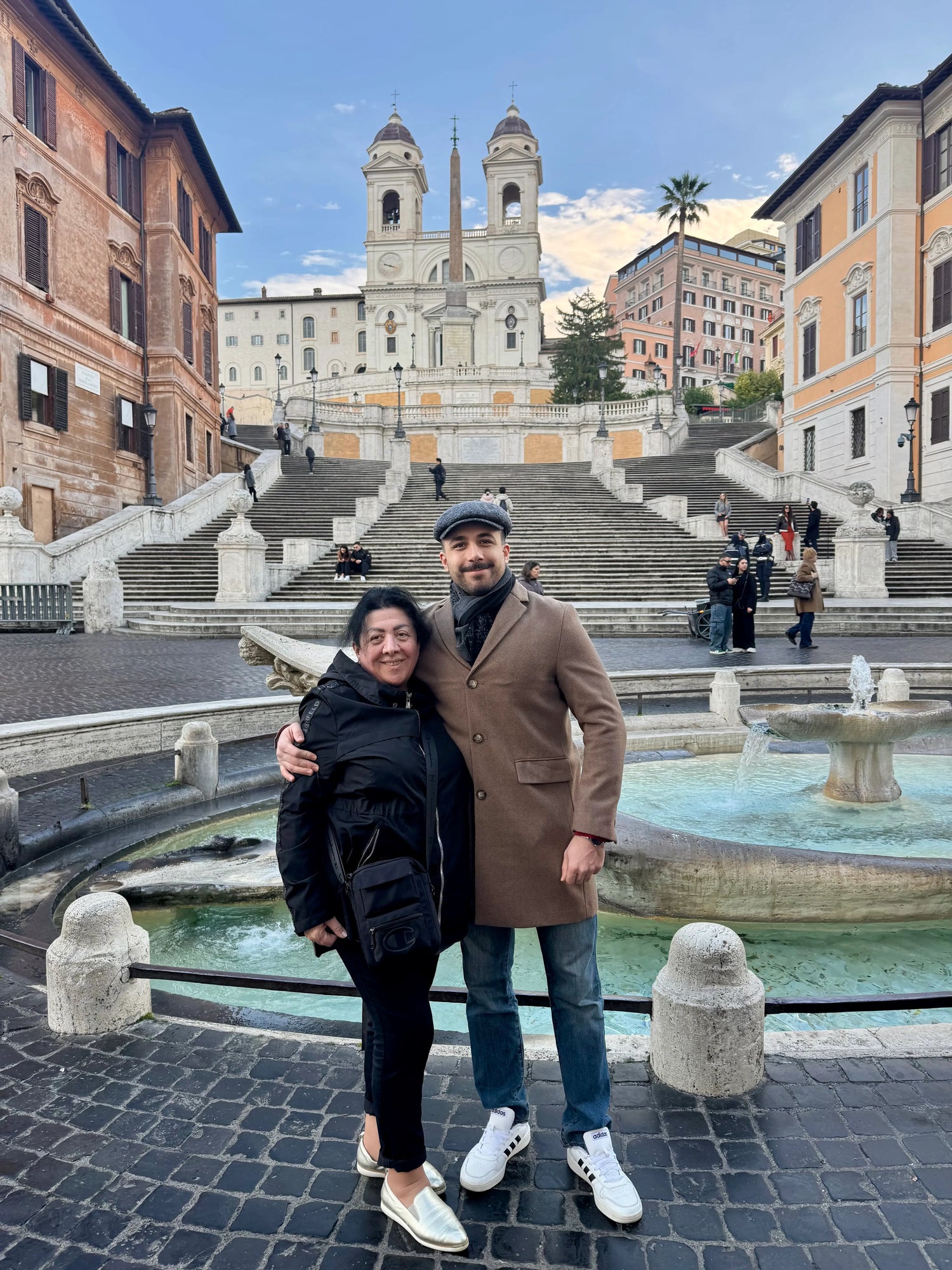 Aygun and her son posing together in front of the famous Spanish Steps in Rome, with a large fountain in the foreground and historic buildings on both sides.