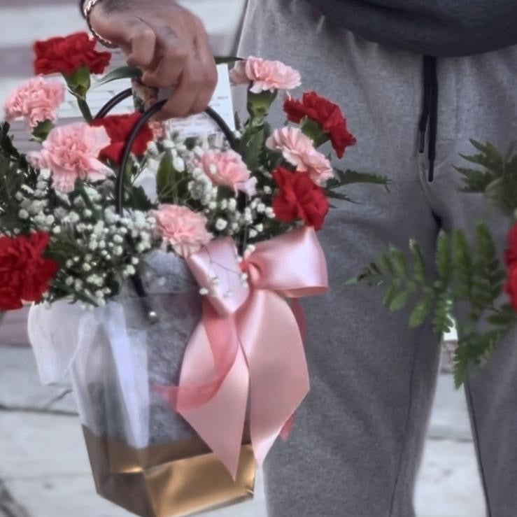 Person holding a bouquet of flowers with a pink ribbon on a blurred background
