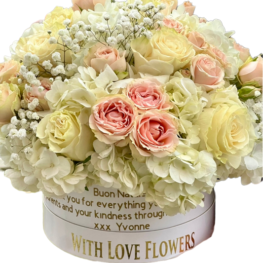 A round white flower box filled with a bouquet of pale cream roses, blush pink roses, and white baby's breath, with printed text on the front. Flower Delivery Toronto.