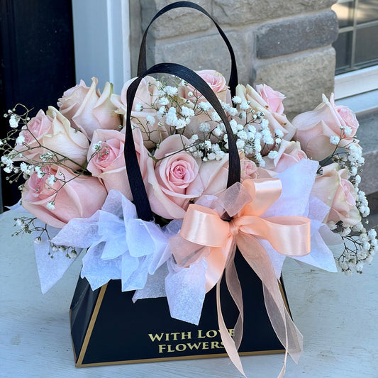 A dozen pink and white roses arranged in a purse-shaped black box with a bow.