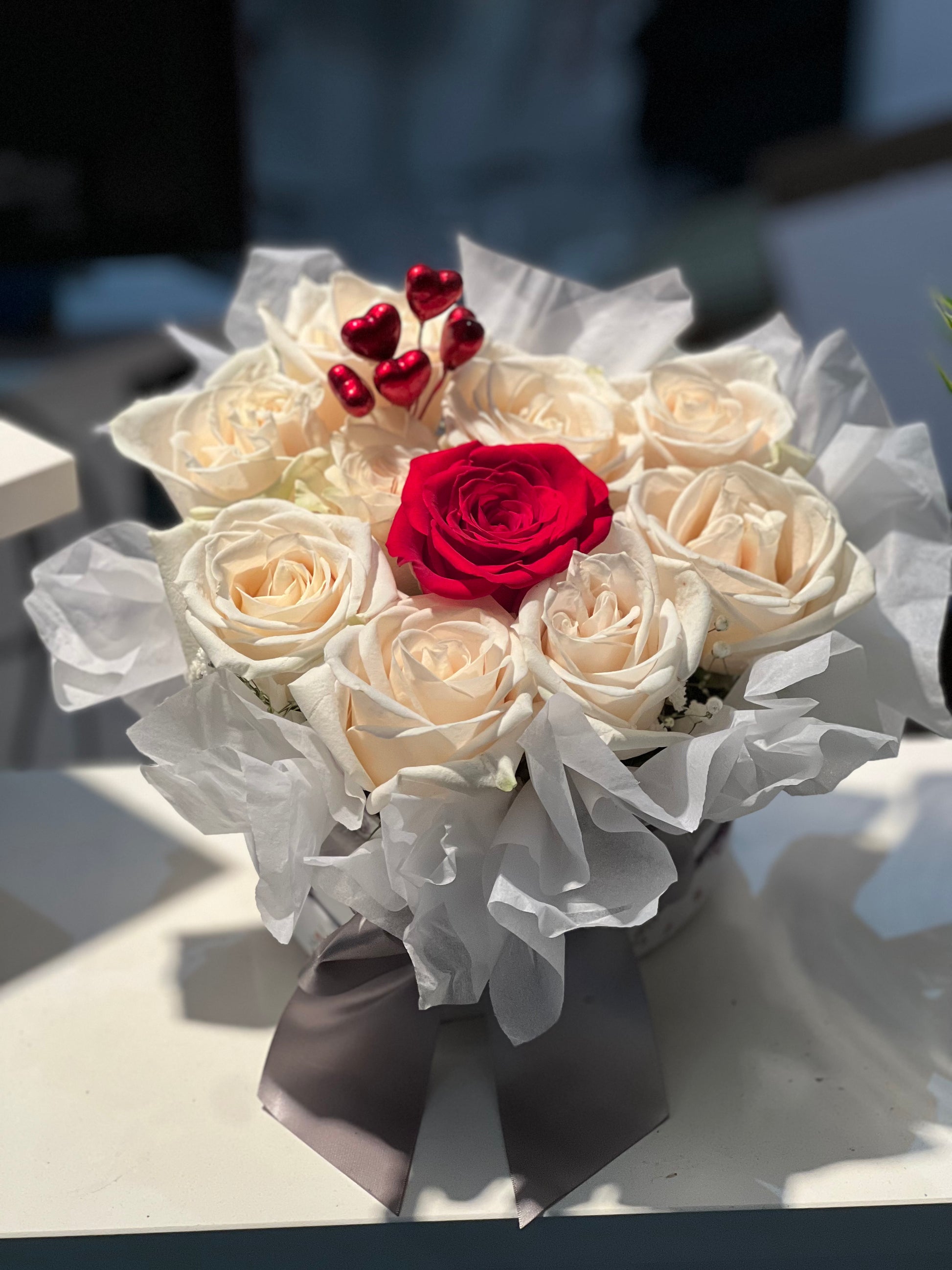 Bouquet of white roses with a red rose in the center on a light surface.