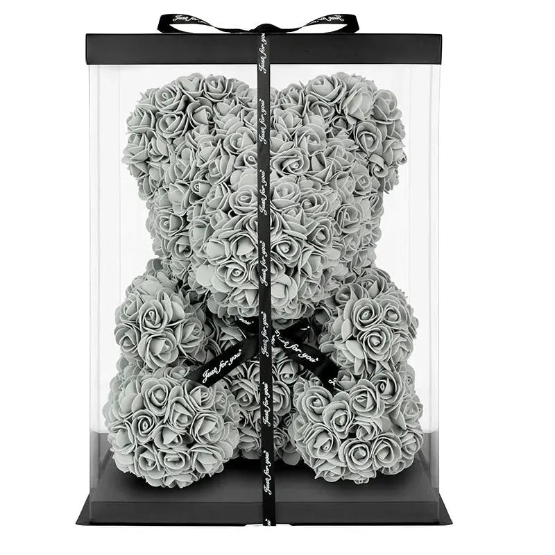 Clear gift box with a black ribbon containing a silver rose teddy bear on a white background