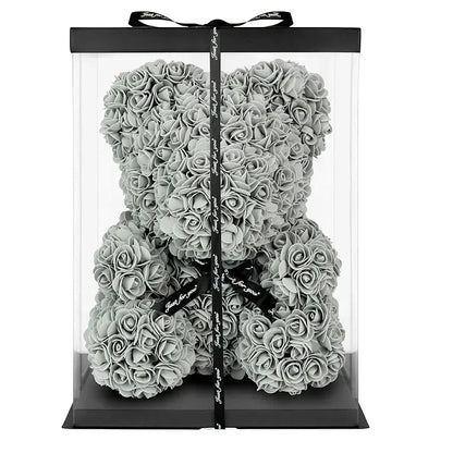 Clear gift box with a black ribbon containing a silver rose teddy bear on a white background