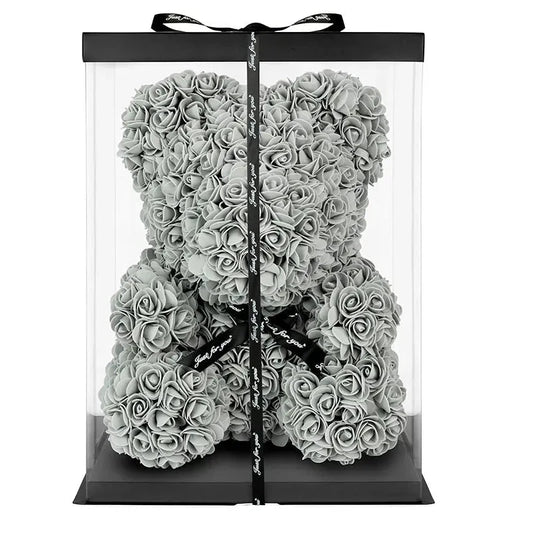 Clear gift box with a black ribbon containing a silver rose teddy bear on a white background