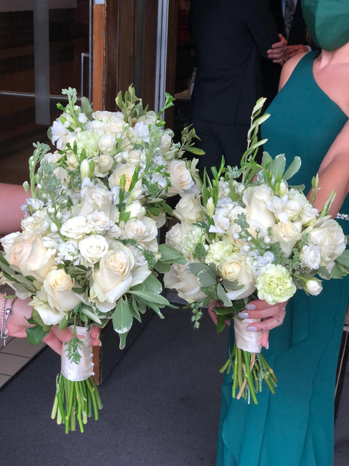 Two bridesmaids holding matching white rose bouquets in a wedding setting, with one wearing a teal dress and the other partially visible on the left.