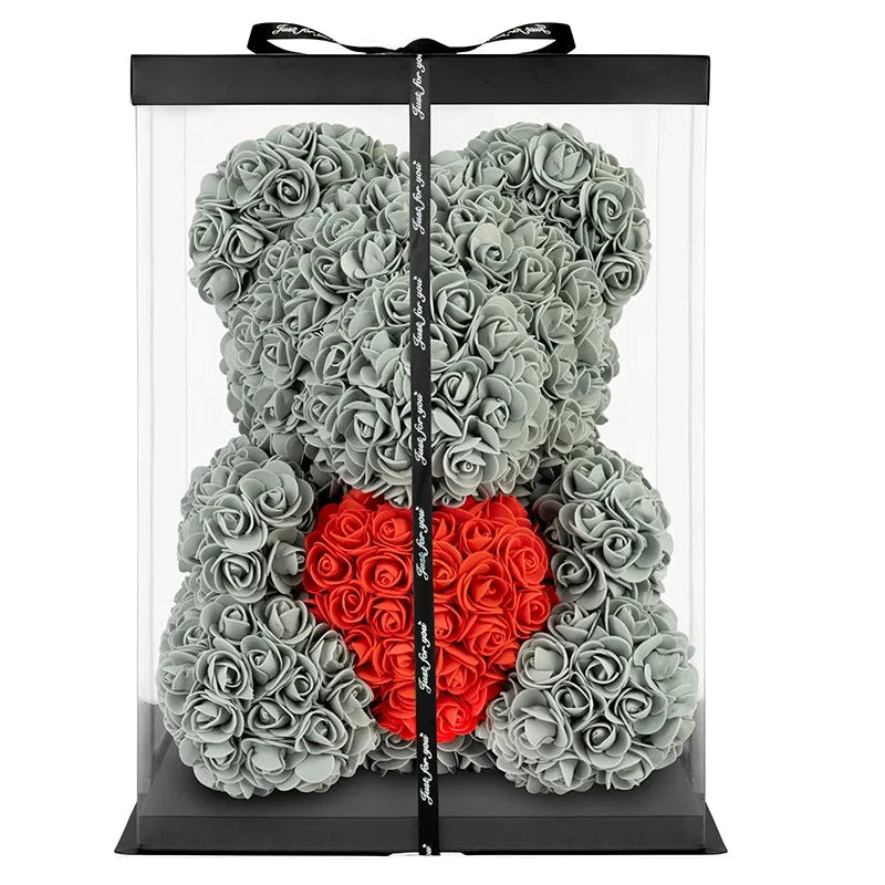 A preserved teddy bear flower arrangement made of gray roses, with a red heart-shaped rose cluster at the center, displayed inside a clear rectangular gift box with a black lid and black ribbon.