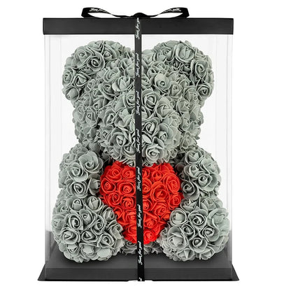 A preserved teddy bear flower arrangement made of gray roses, with a red heart-shaped rose cluster at the center, displayed inside a clear rectangular gift box with a black lid and black ribbon.